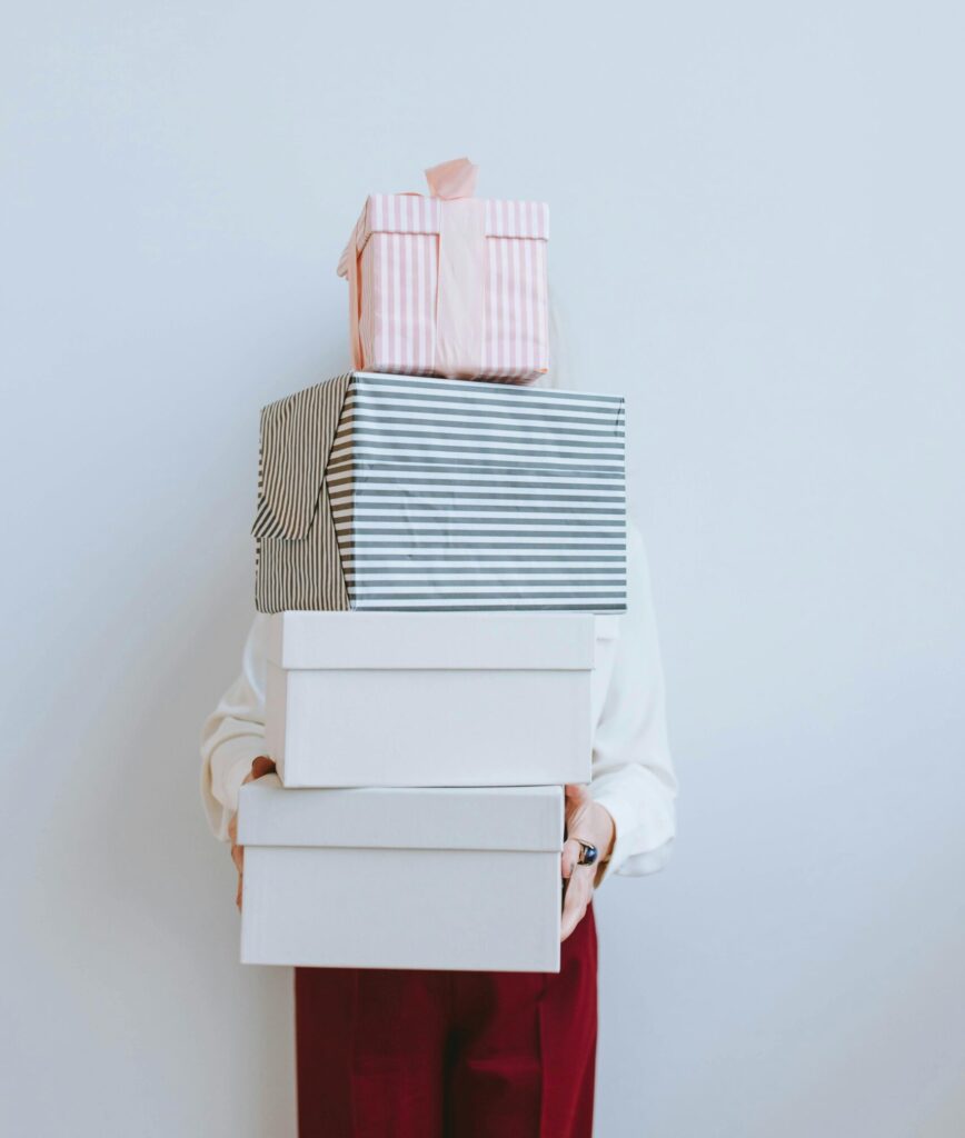 A person holding a pile of gift boxes wrapped in striped paper, wearing striking red pants.